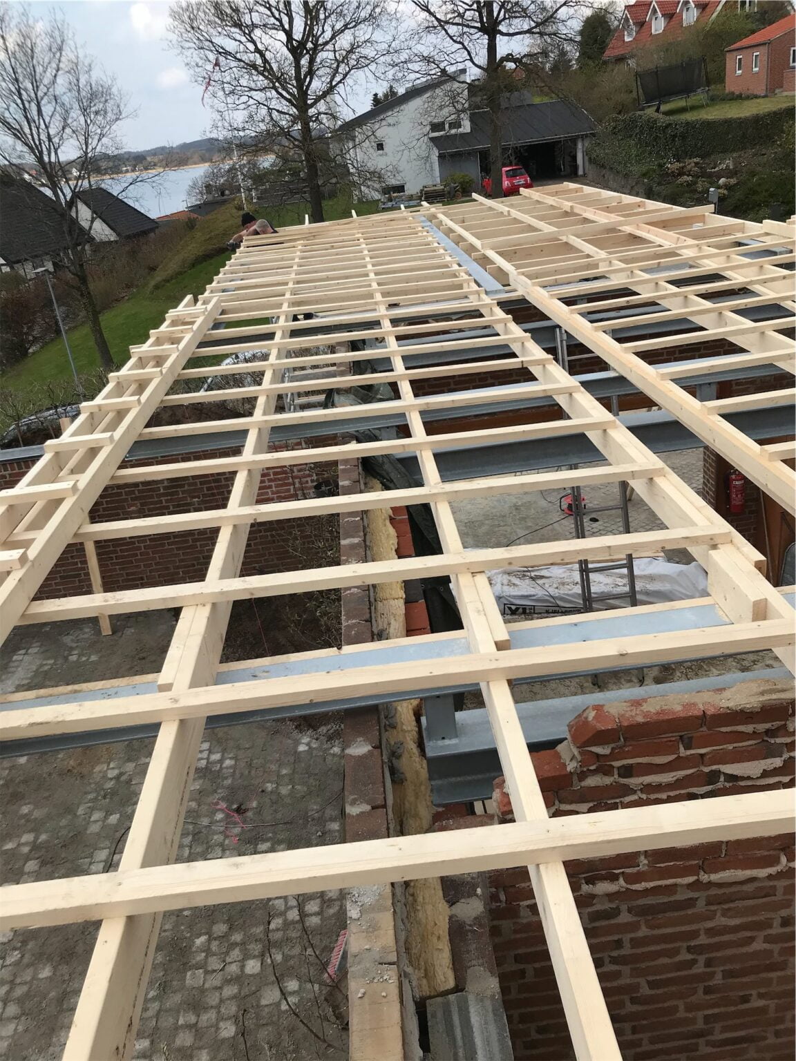 Trækonstruktion på byggeplads nær sø og huse.